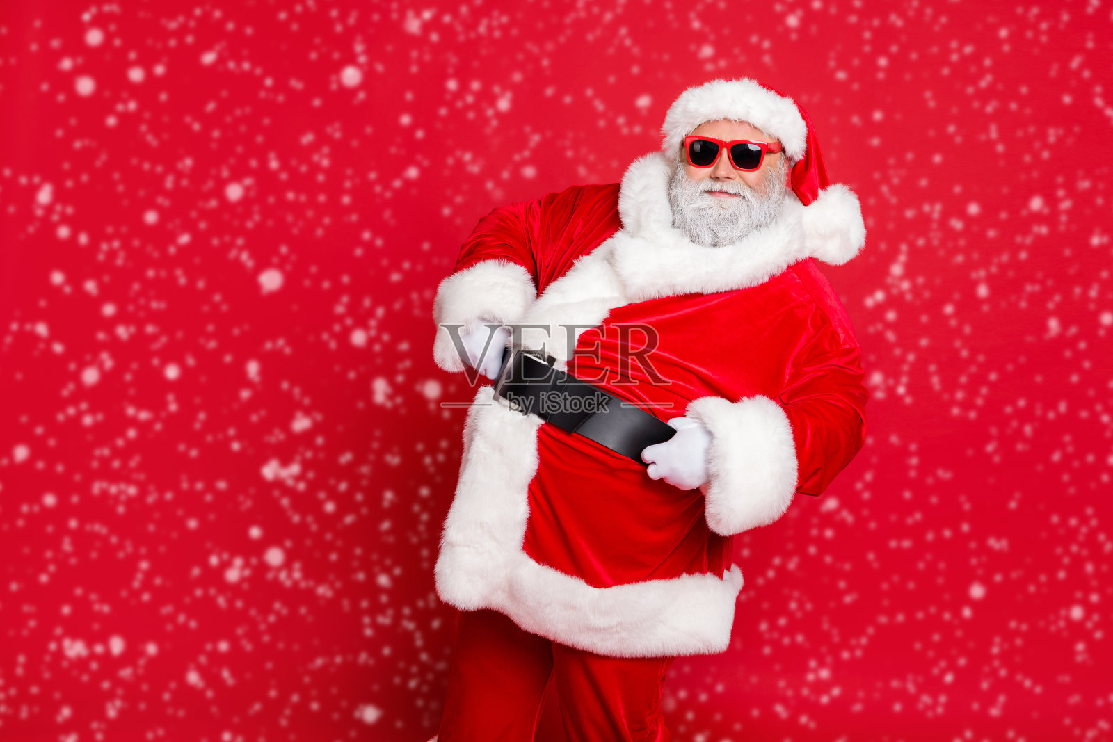 Portrait of his he nice attractive cheerful cheery content bearded Santa showing eve noel festive festal mood holding belt isolated over bright vivid shine red background照片摄影图片