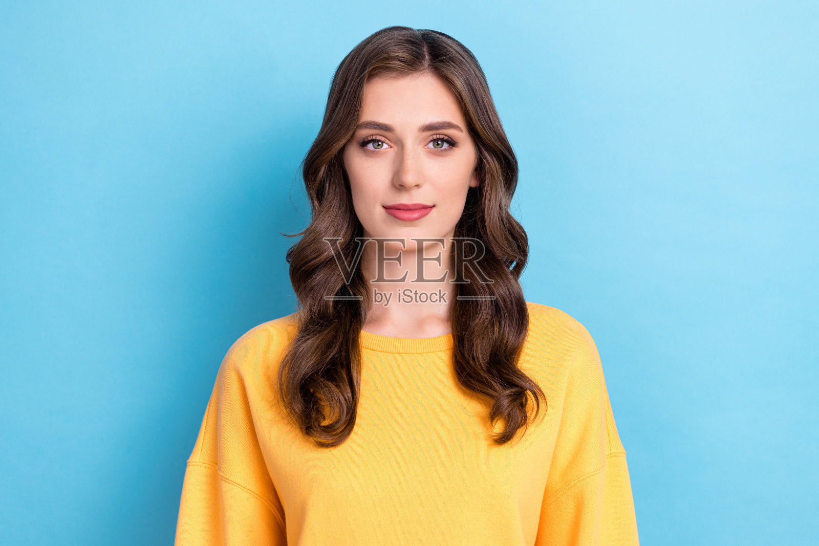 特写照片：年轻可爱、漂亮、友好的女性，穿着黄色毛衣，自信的职场女性，卷发，成功，背景为蓝色。照片摄影图片
