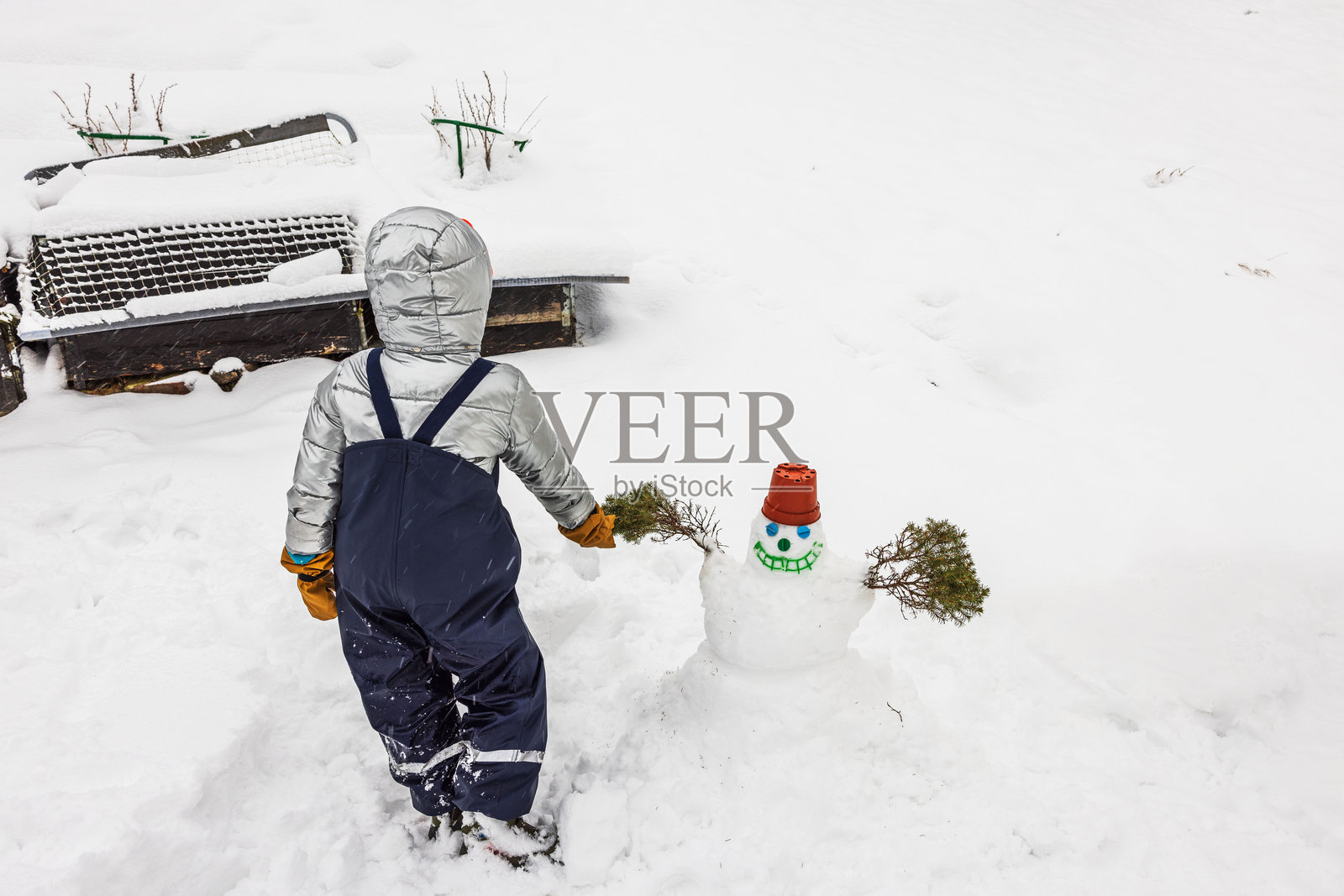 穿着冬季雪服的孩子在瑞典别墅的后院里用锅做帽子堆小雪人。照片摄影图片