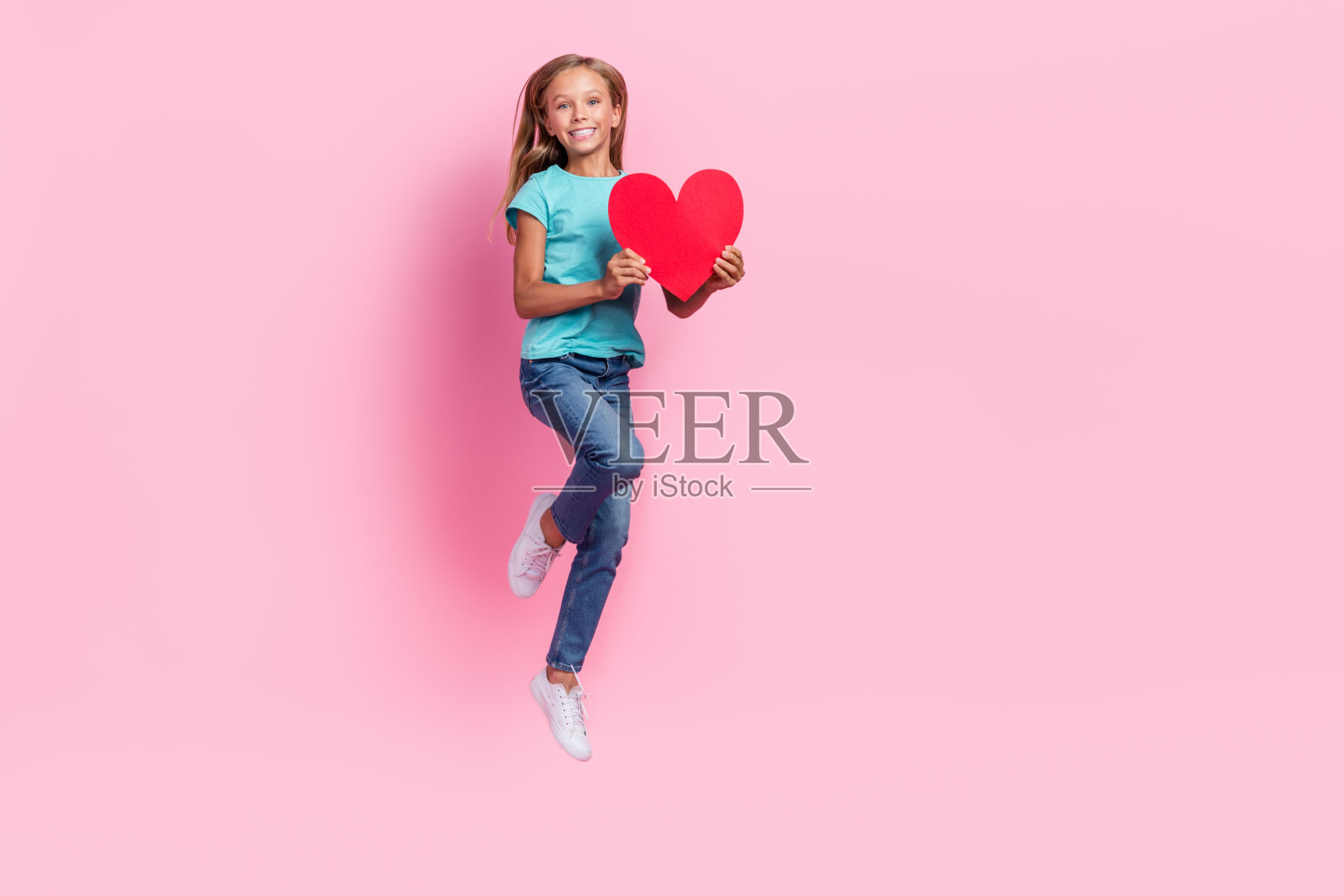 穿着青色T恤的快乐小孩在粉色背景上高高跳起，心中充满喜悦，周围是空旷的空间。照片摄影图片