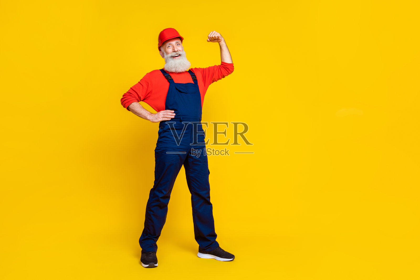自信的工人祖父在明亮的背景下展示肱二头肌，修理建筑物的全身照片照片摄影图片