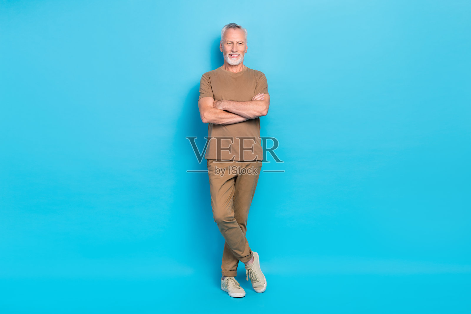 愉快的老年人全身肖像，双臂交叉，心情愉悦，背景为蓝色。照片摄影图片