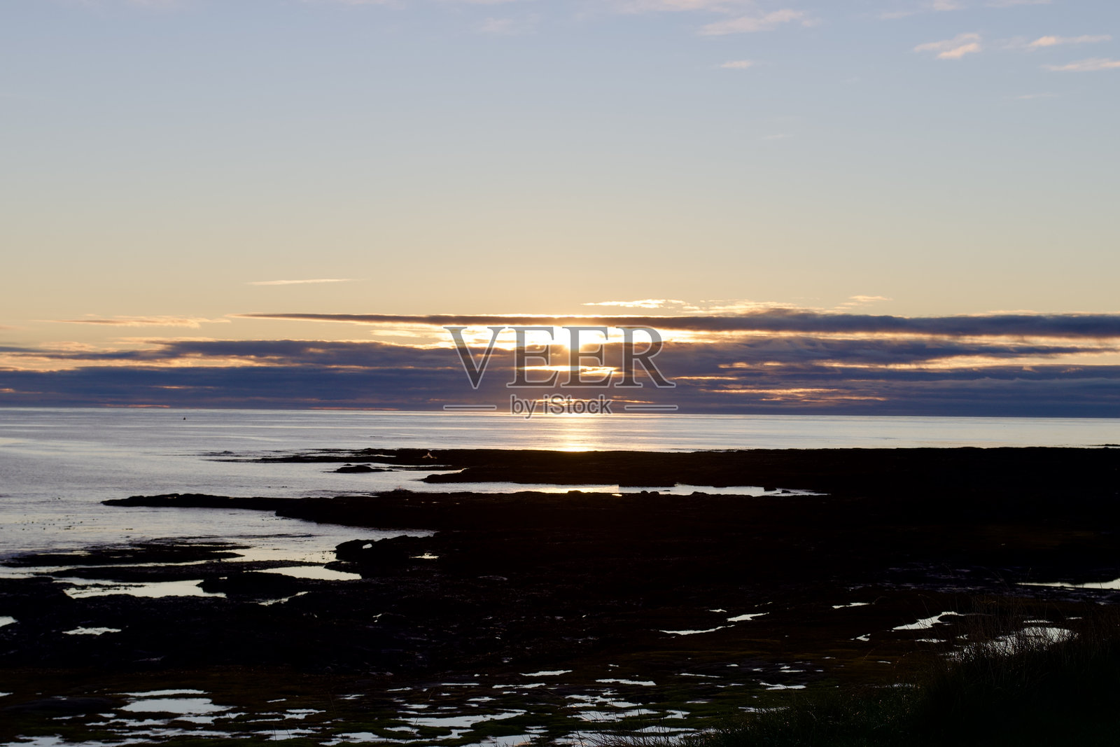海洋和岩石下的日出。金色的天空映衬着黑色的轮廓岩石。照片摄影图片