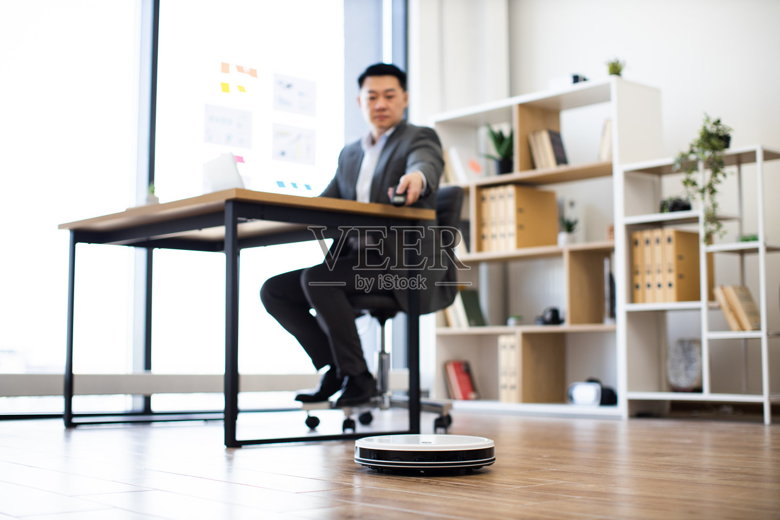 亚洲商人在办公室中与机器人吸尘器多任务处理照片摄影图片