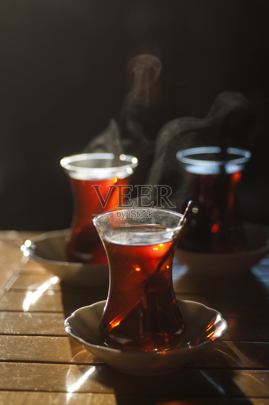美丽的逆光照片，浅景深，热腾腾的土耳其茶在传统玻璃杯中盛放，摆放在木桌上。照片摄影图片