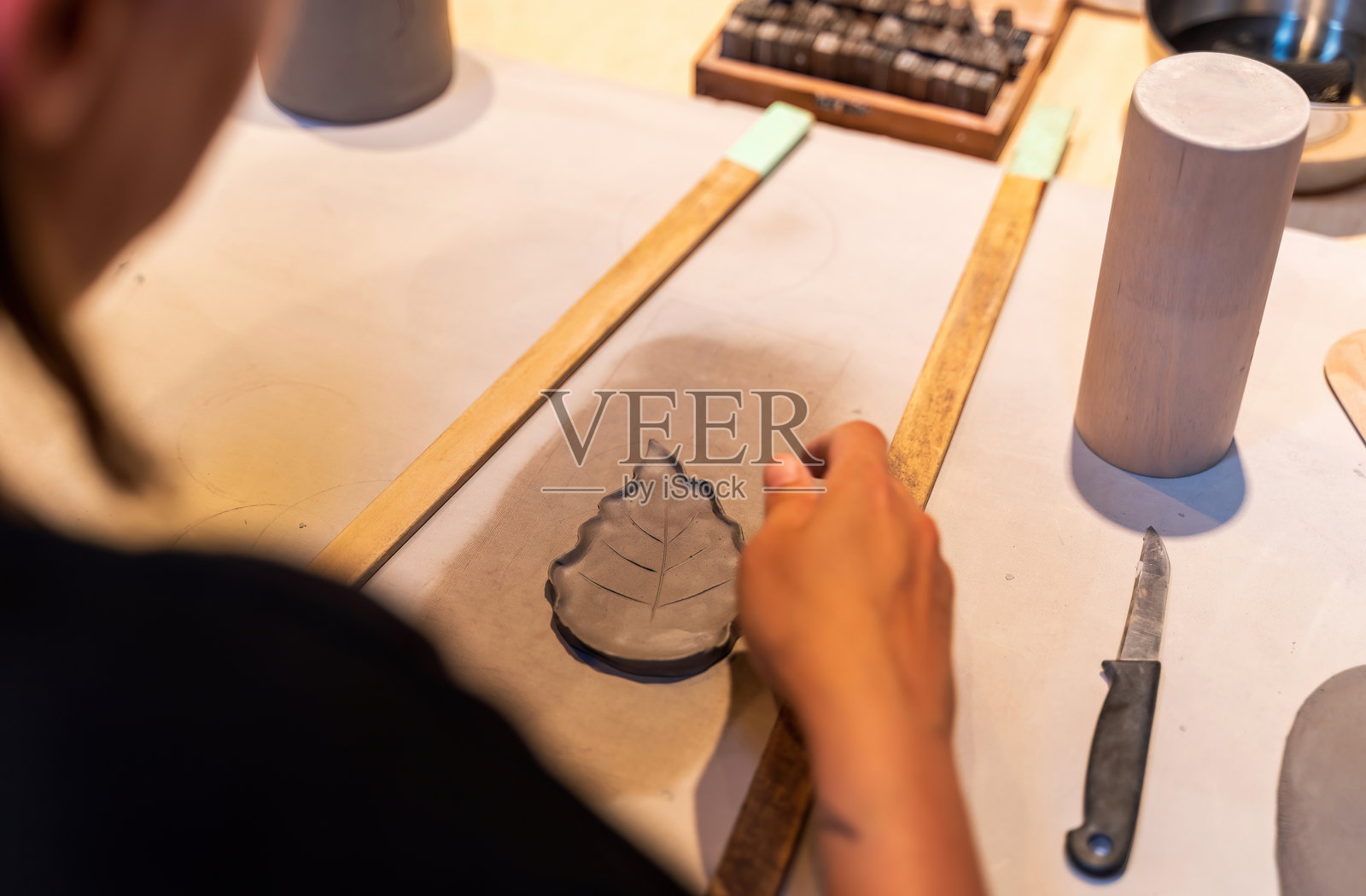 一位工匠在工作室中小心地塑造一个陶瓷叶子，展现出创造力和对细节的关注。照片摄影图片