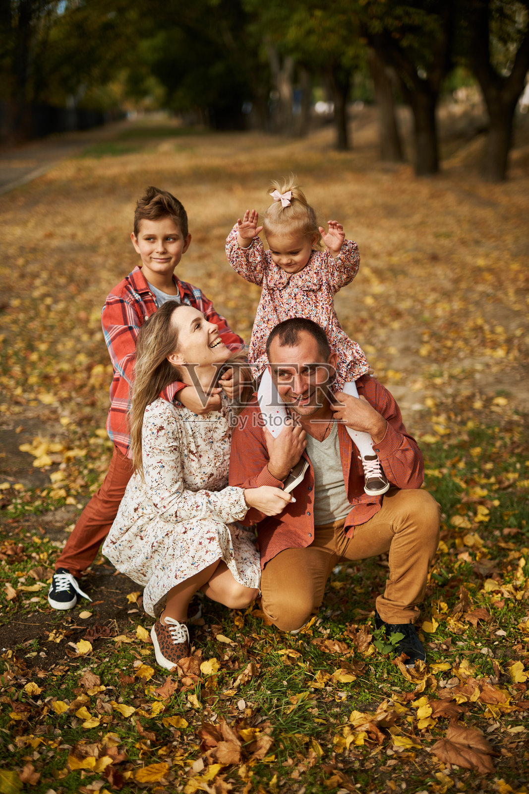 快乐的家庭在秋天的公园里走在铺满落叶的草地上。照片摄影图片