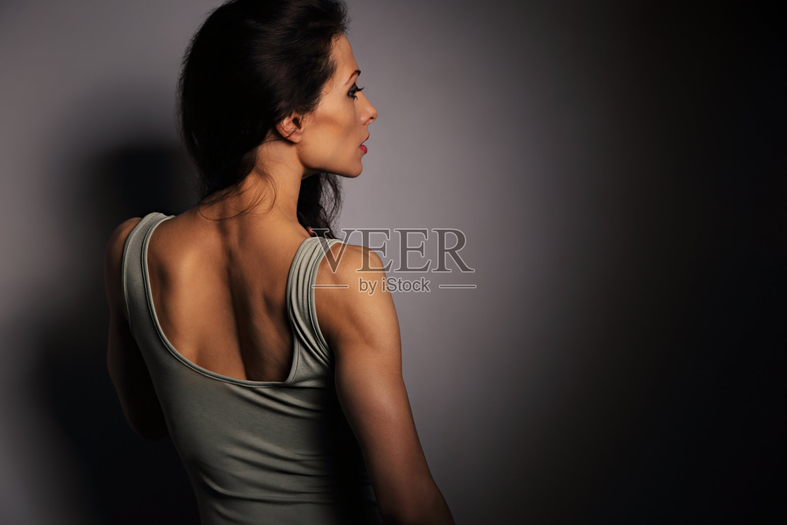 美丽的体操瘦女人，长发，运动强健的身体，半影与光线映照在工作室墙壁背景上。特写，留有空白空间。艺术。侧面背影。照片摄影图片