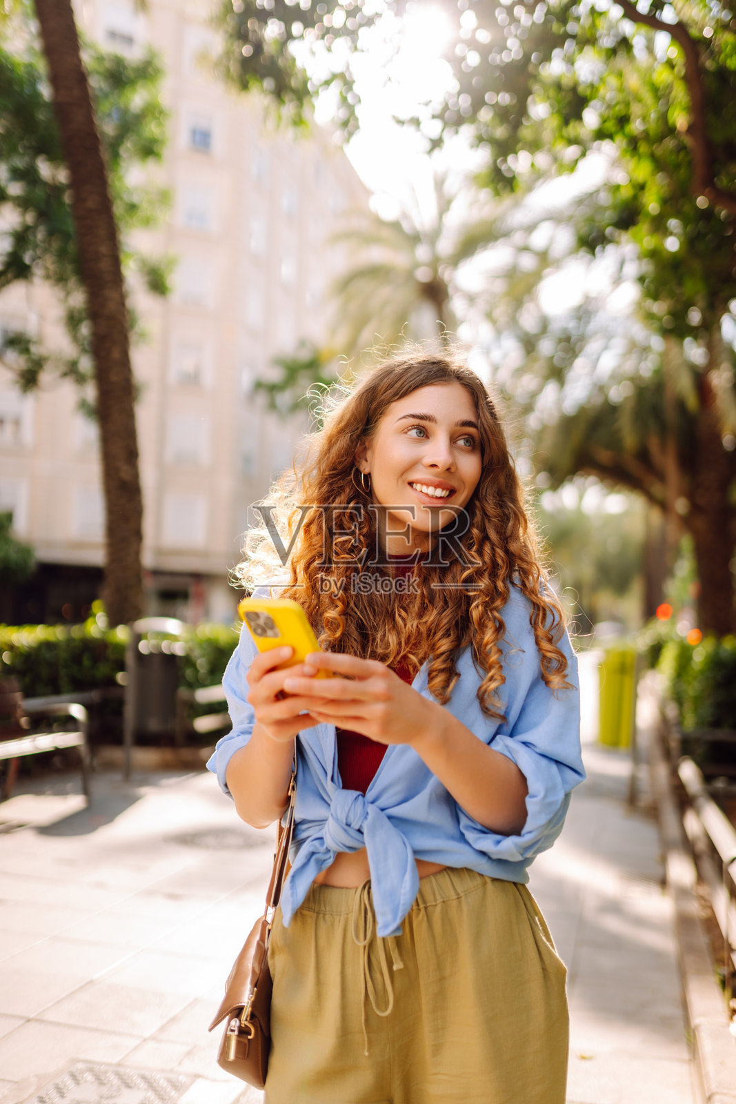 年轻女性在城市中走路，手里拿着手机。照片摄影图片