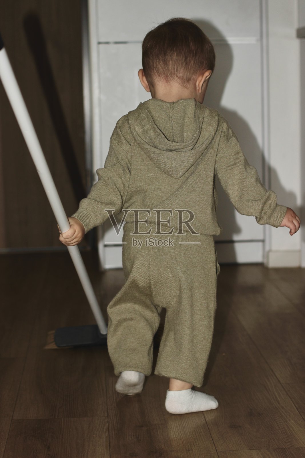 一个小孩在房间里手里拿着扫帚。小熊正在努力清理。照片摄影图片