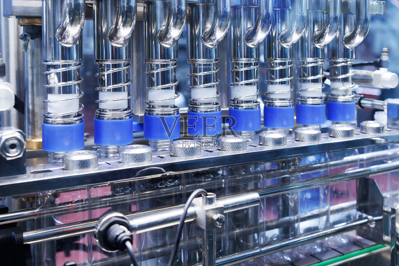 机器人手臂将塑料瓶移动到化妆品和护肤品制造的自动封盖和贴标机的传送带上。化妆品行业与人工智能技术机械概念。照片摄影图片