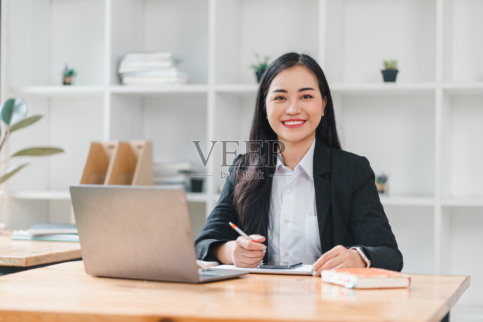自信的女商人在办公桌前微笑，展示现代办公环境。她专注于笔记本电脑和笔记，体现出专业和高效。照片摄影图片