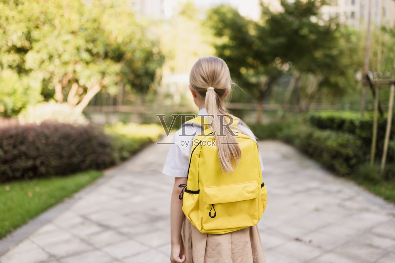 回到学校。小女孩背着黄色书包在户外。照片摄影图片