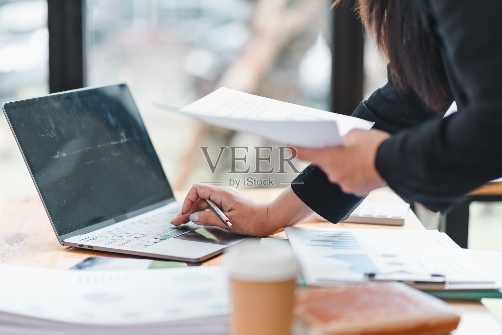 一个人正在使用笔记本电脑，同时手里拿着文件，周围是办公材料，传达出一种高效和专注的感觉。照片摄影图片