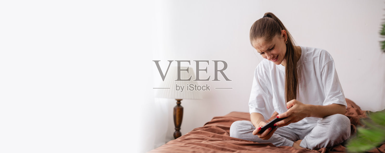 棕发女性在卧室里享受玩手机游戏的乐趣照片摄影图片