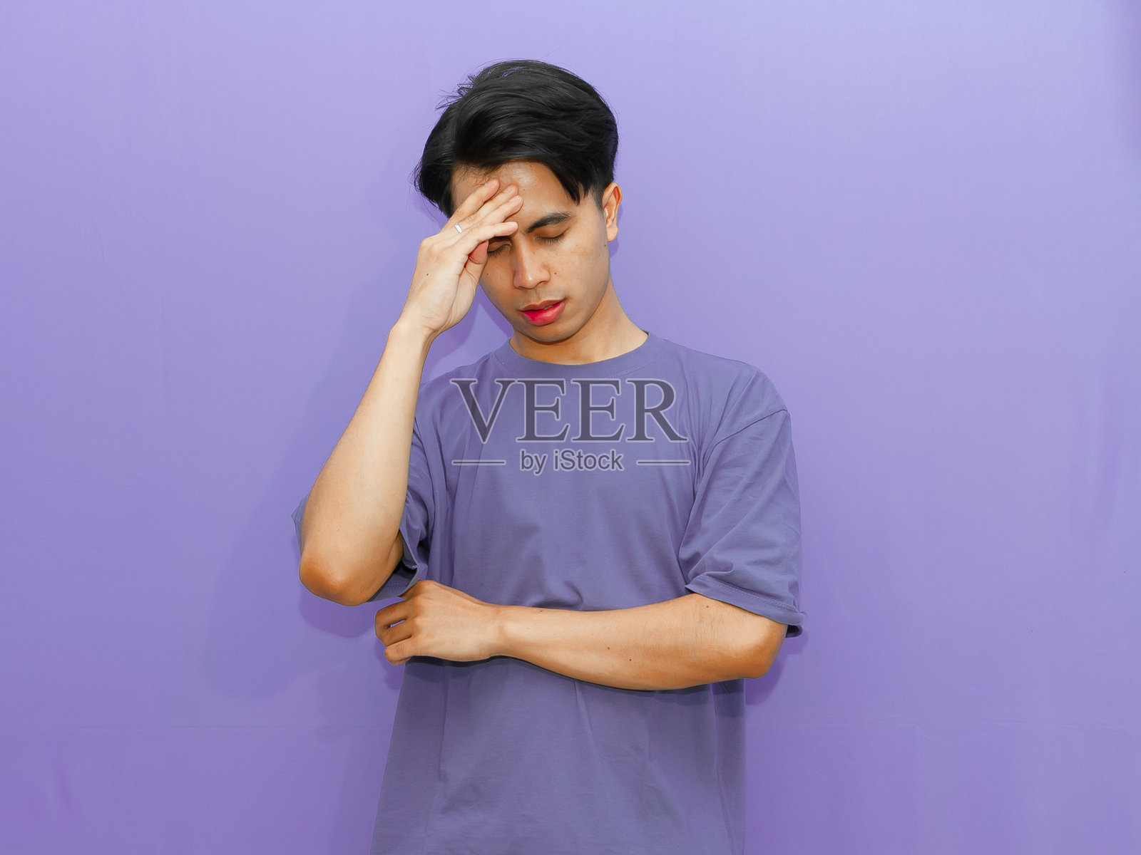一位年轻的亚洲男性在紫色背景下按摩头部，表现出压力和疼痛。照片摄影图片