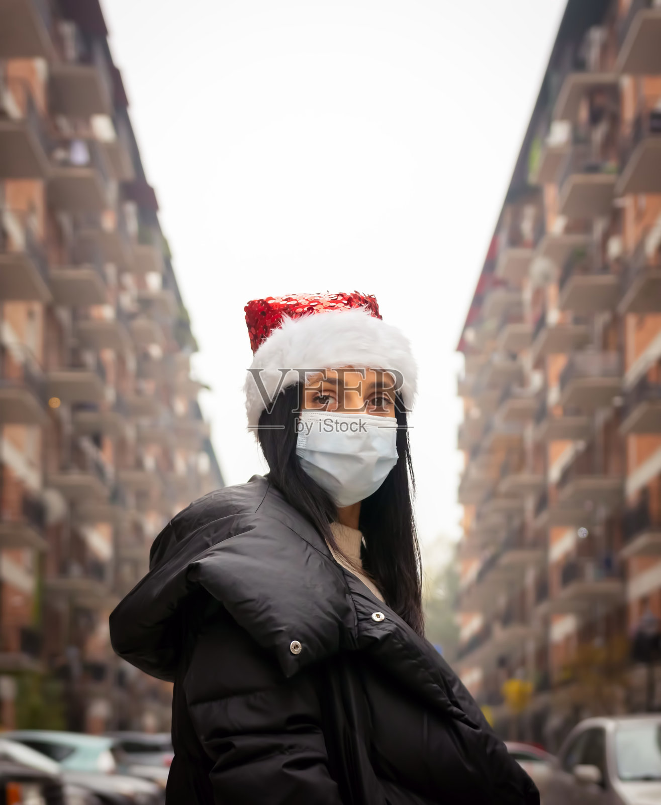 女人戴着圣诞帽站在街道上，周围是方块形的房屋。圣诞节季节假日概念照片摄影图片