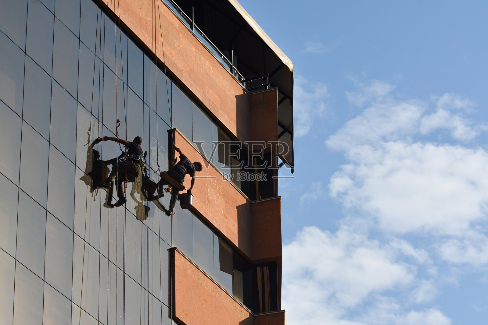 一群工人在现代办公大楼的脚手架上清洁窗户。照片摄影图片