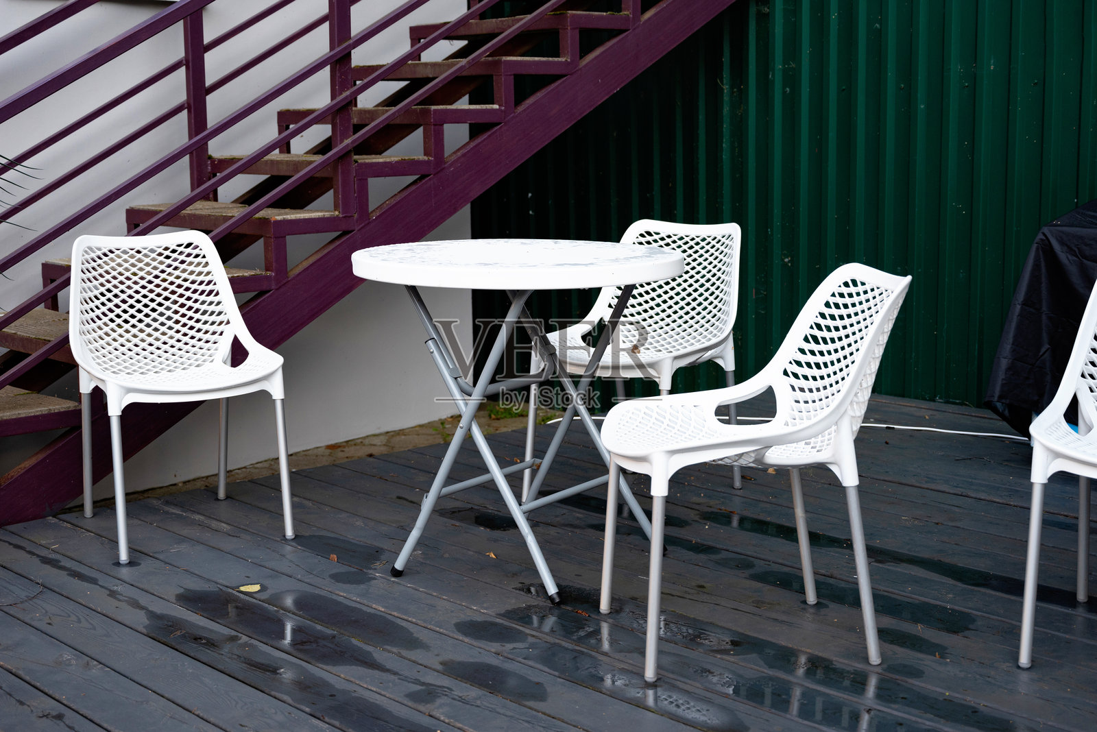 户外座位区，白色椅子和桌子放在湿润的木质甲板上。照片摄影图片