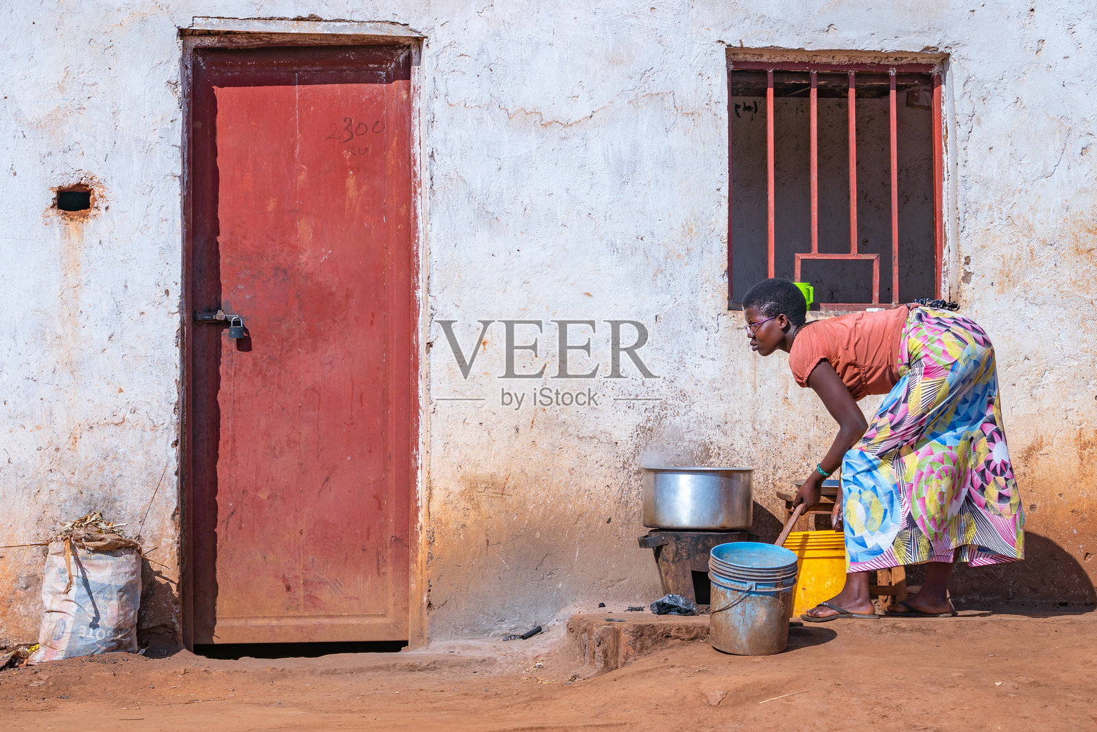 一位穿着色彩斑斓裙子的女性站在一扇引人注目的红色门前,布隆迪照片摄影图片