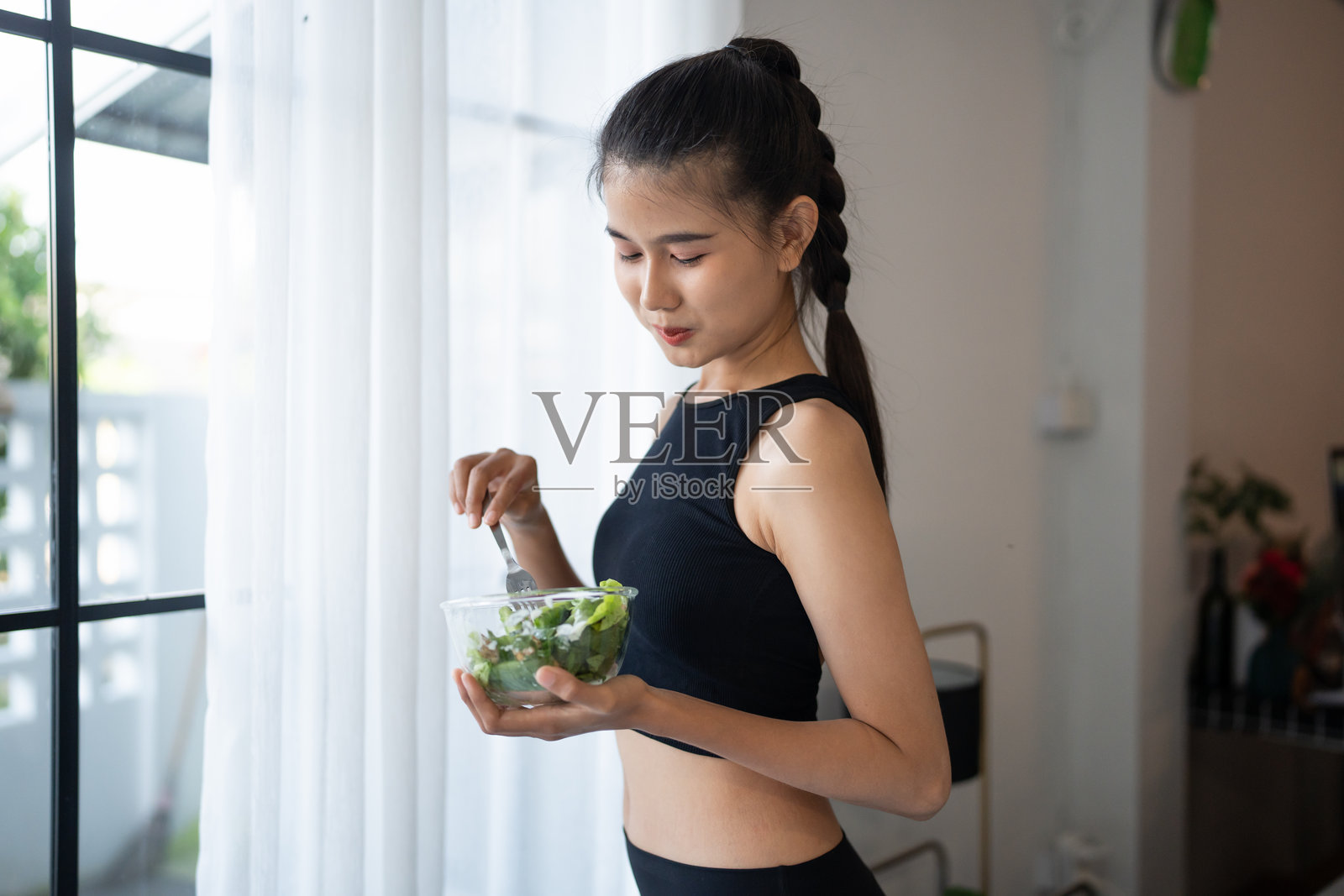 健身的亚洲女性在锻炼后享用健康沙拉，微笑着。美丽的年轻亚洲女性在瑜伽馆里锻炼后吃健康食品，展现健康的生活方式。照片摄影图片