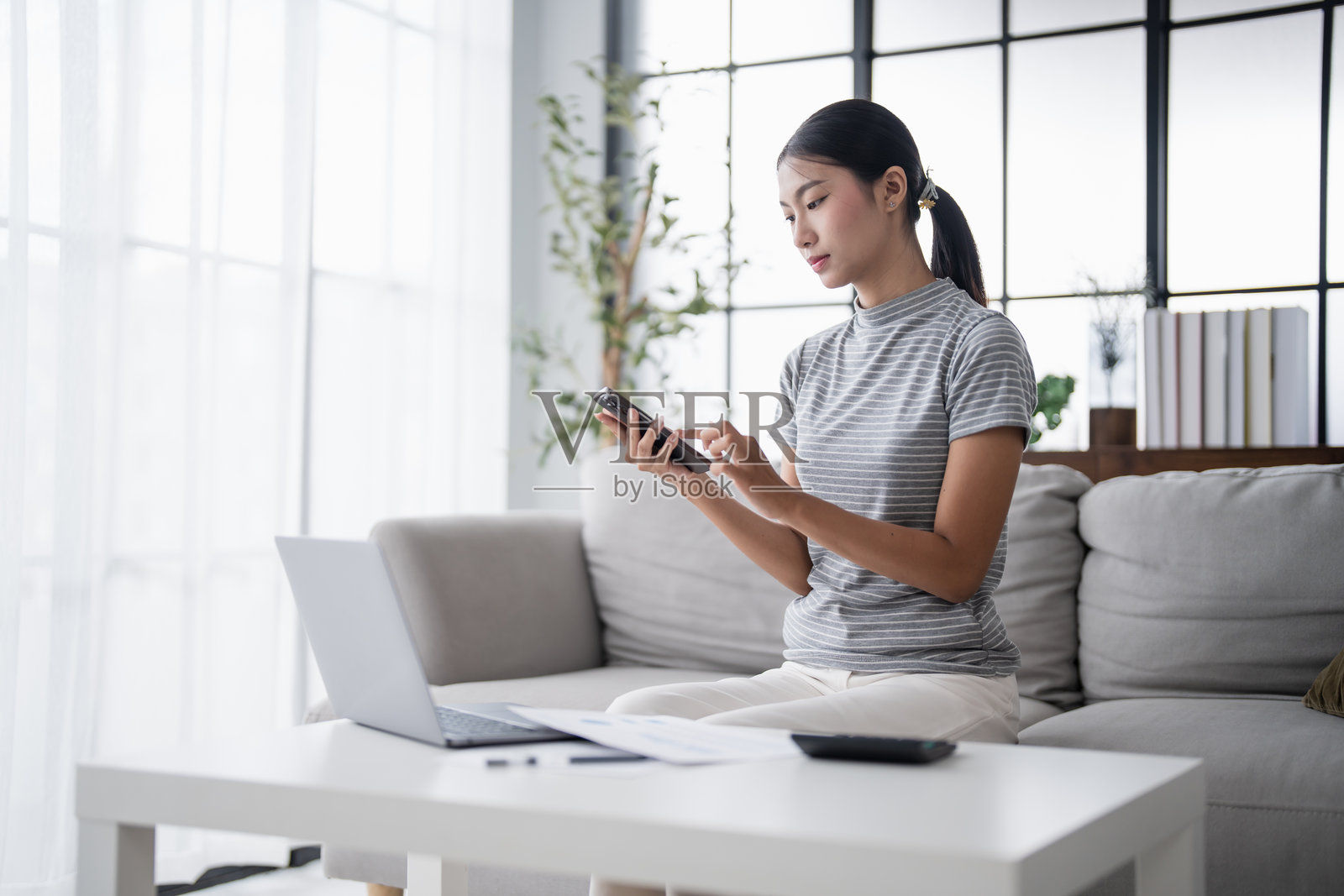 亚洲女性手持纸质文件，通过手机应用计算储蓄、支付账单，使用智能手机在线支付家庭账单、税费和保险，管理预算。照片摄影图片
