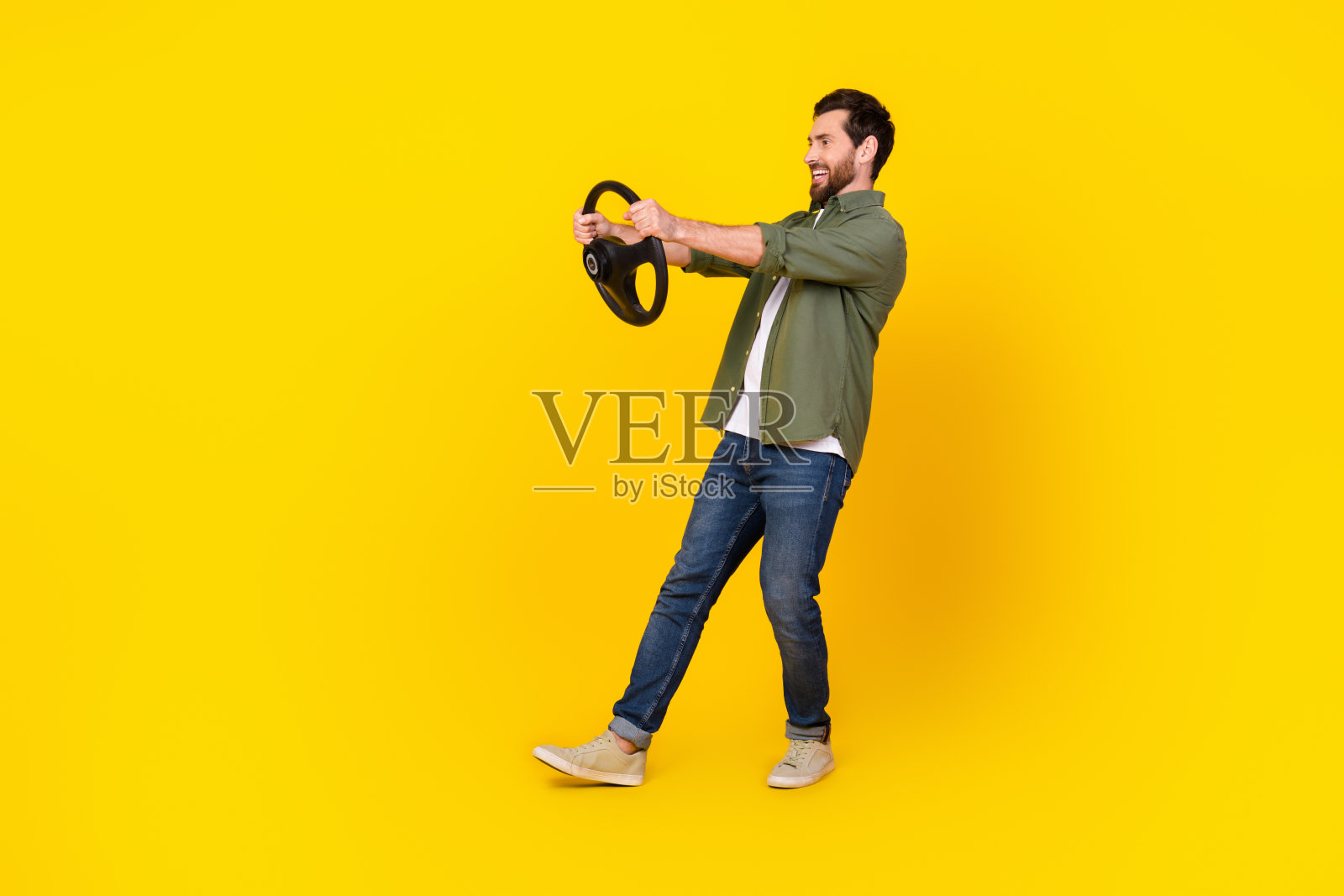 年轻男子全身肖像，手握方向盘，穿着衬衫，背景为黄色，空旷无物。照片摄影图片