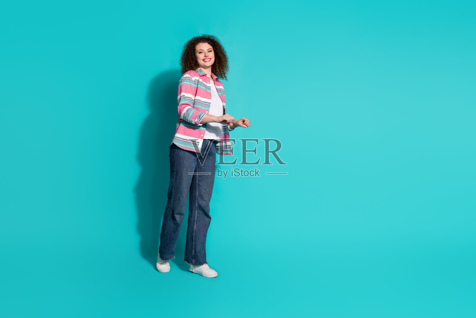 全身肖像，年轻女性穿着衬衫，手推空购物车，背景为青绿色。照片摄影图片