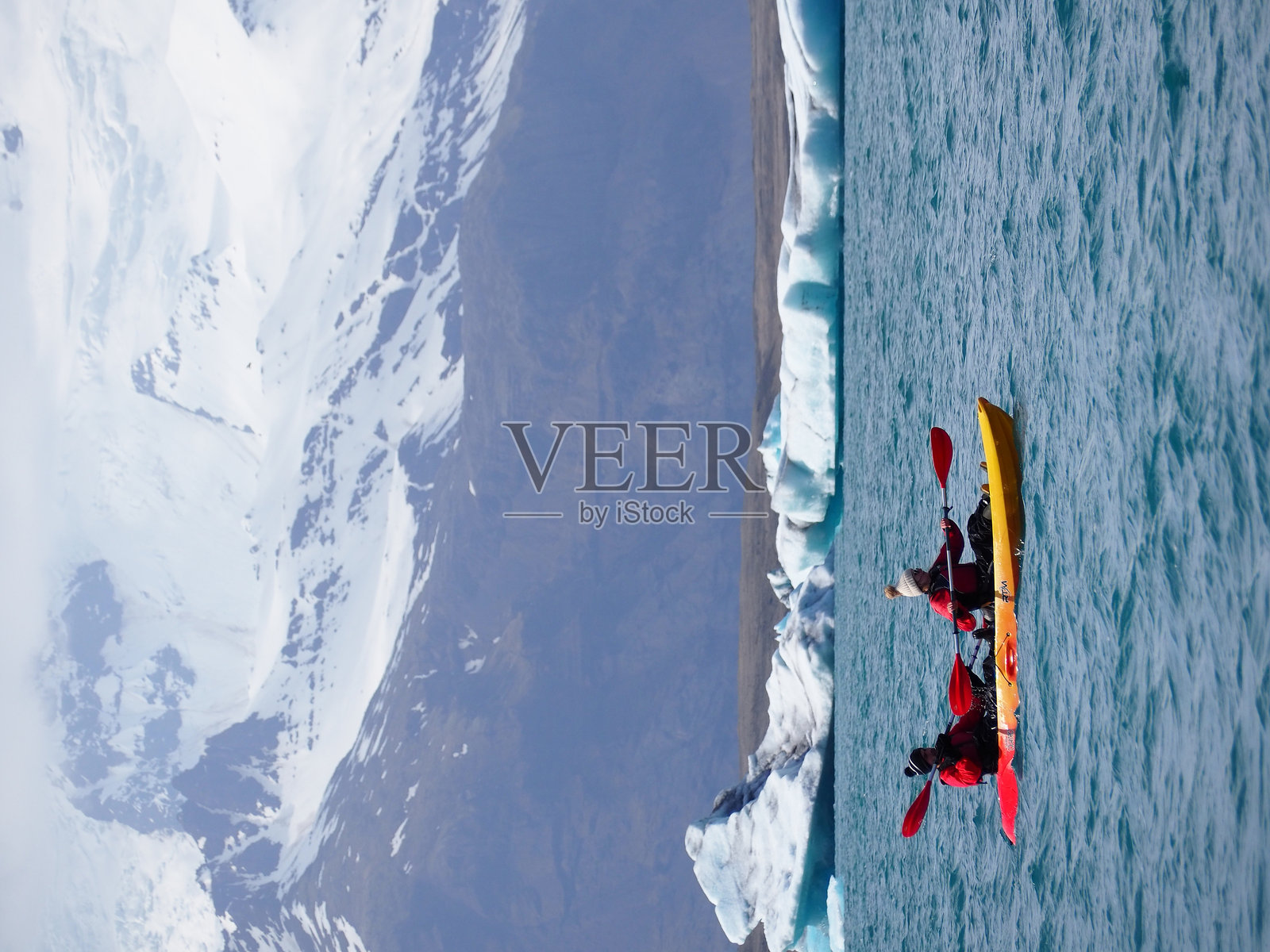 冰岛的杰古沙龙湖 - 2024年5月16日：照片展示了人们在清澈的冰川水域中划皮艇，背景是雪山和冰山。照片摄影图片