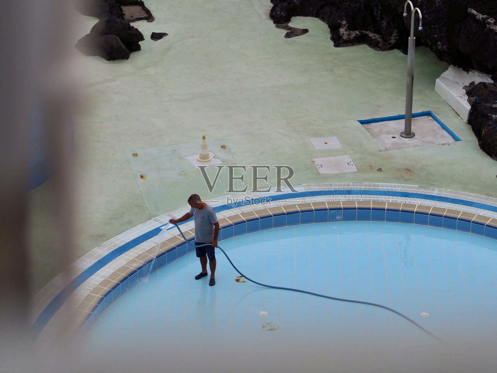 葡萄牙马德拉 - 2024年10月20日：在清晨时分，一名孤独的男子在宁静的背景下，细致入微地清洁游泳池，融合了责任与宁静。照片摄影图片