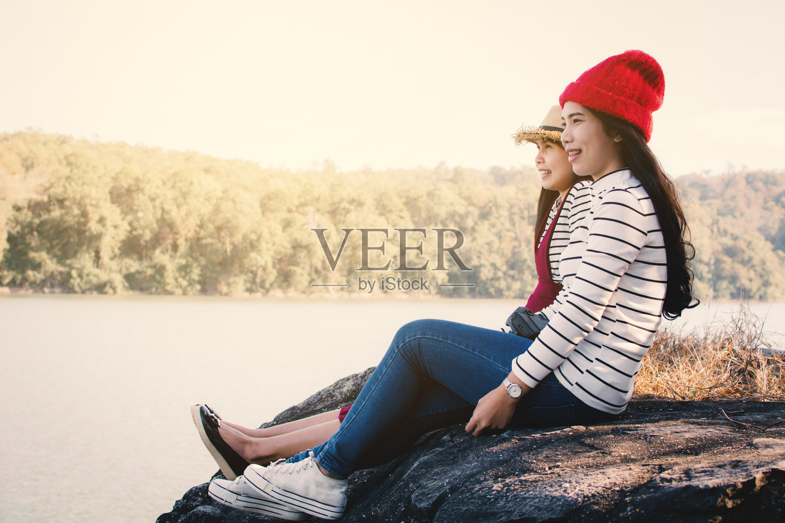 边看微笑的朋友坐在岩石上看湖照片摄影图片