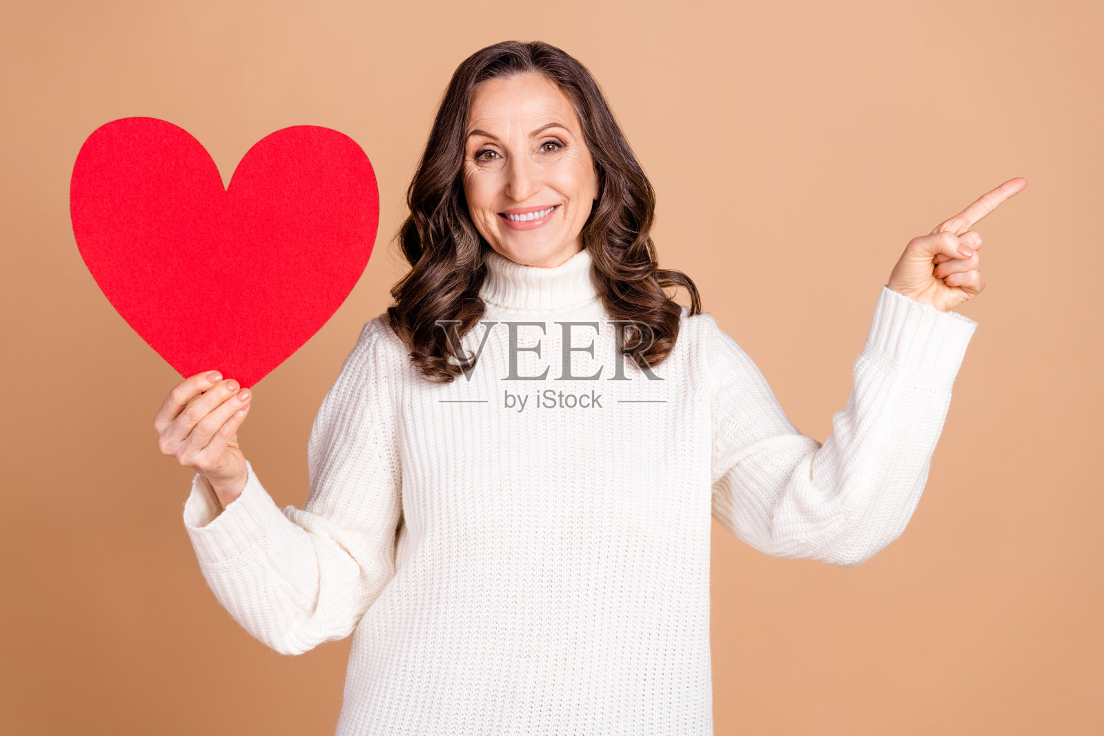 可爱的女性退休人员穿着时尚服装，展示空白空间，背景为米色。照片摄影图片