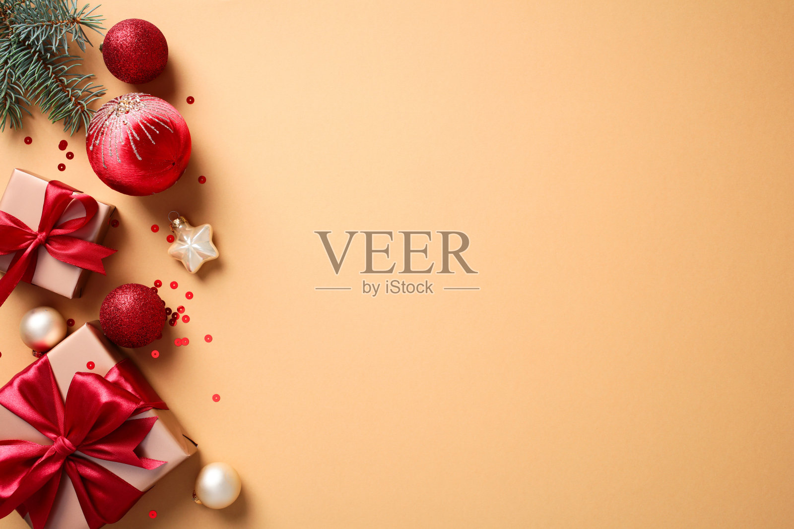 圣诞节平铺图，包含用红色丝带装饰的礼品盒、松枝、饰品和星星，背景为米色。非常适合节日营销、贺卡和季节性设计。照片摄影图片