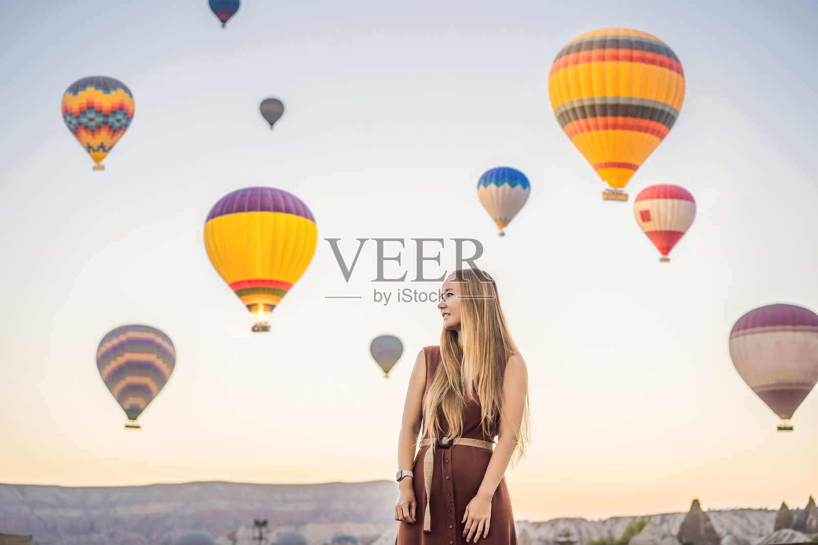 在土耳其卡帕多奇亚，一位女游客欣赏热气球。快乐的土耳其旅行概念。女人在山顶享受美妙的景色。照片摄影图片