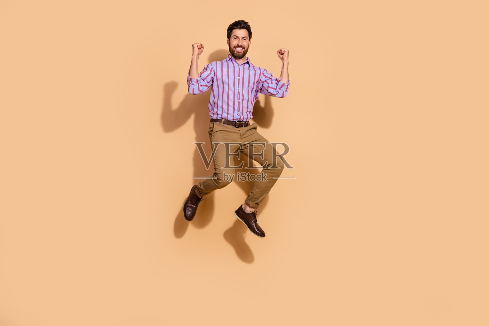 穿着正式服装的成年人跳起，双拳高举，展示团队精神，背景为米色。照片摄影图片