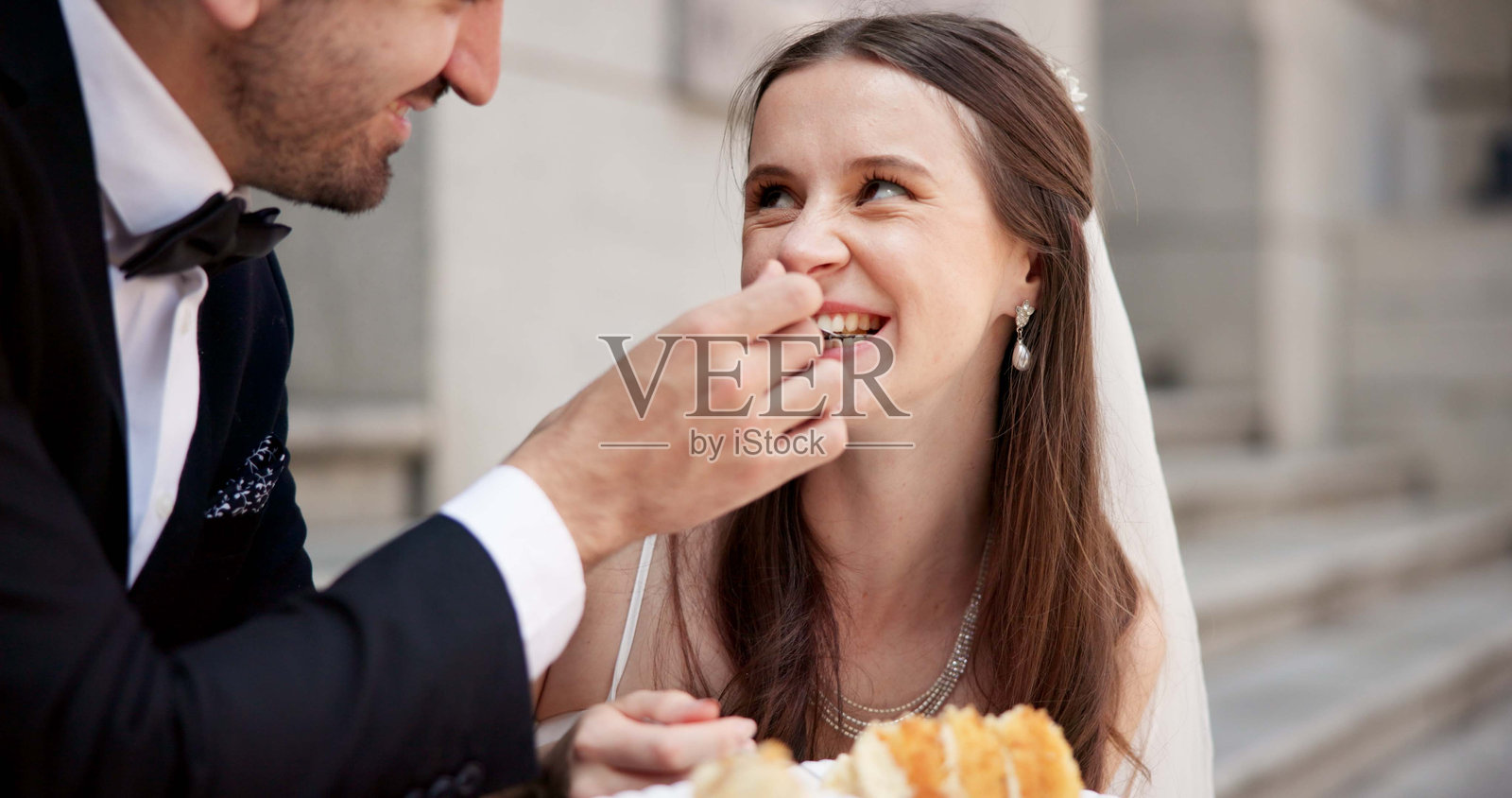 城市中的微笑情侣在婚礼上与蛋糕，幸福的新娘与新郎在街道上一起。城市浪漫，男女在民事婚礼活动中，户外庆祝时分享甜点。照片摄影图片