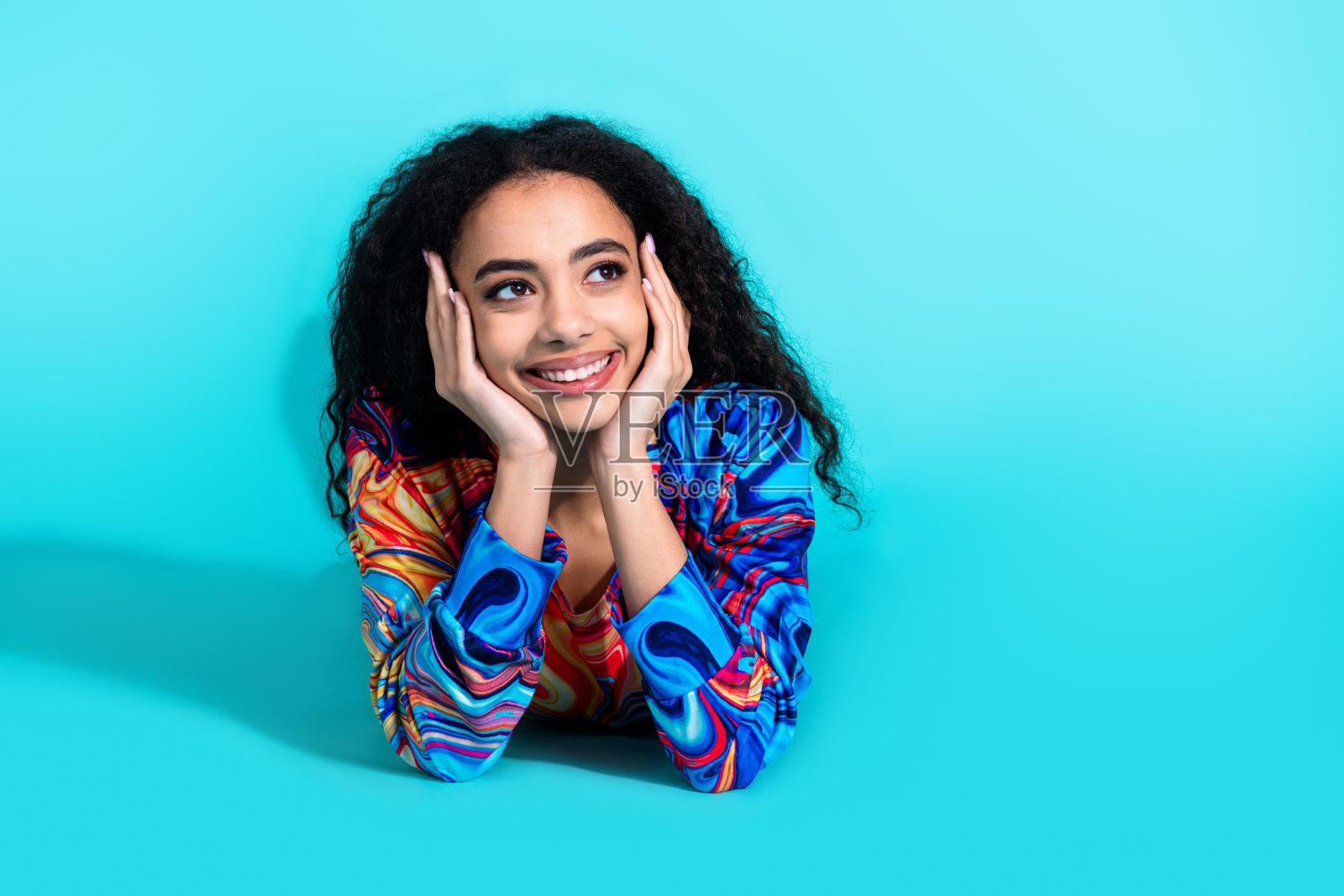 漂亮年轻女孩躺在地板上，望着空旷的空间，穿着毛衣，背景为青绿色。照片摄影图片