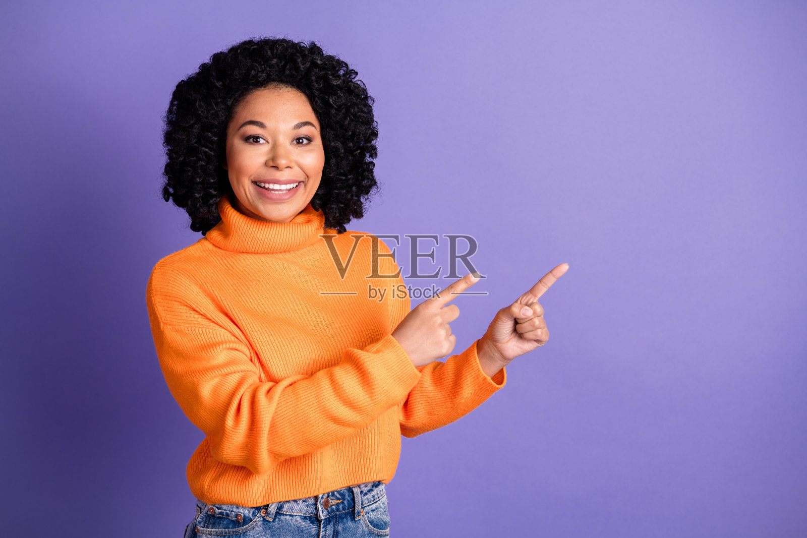 穿着针织毛衣的快乐漂亮女士在紫色背景前展示两个手指，旁边留有空白空间。照片摄影图片