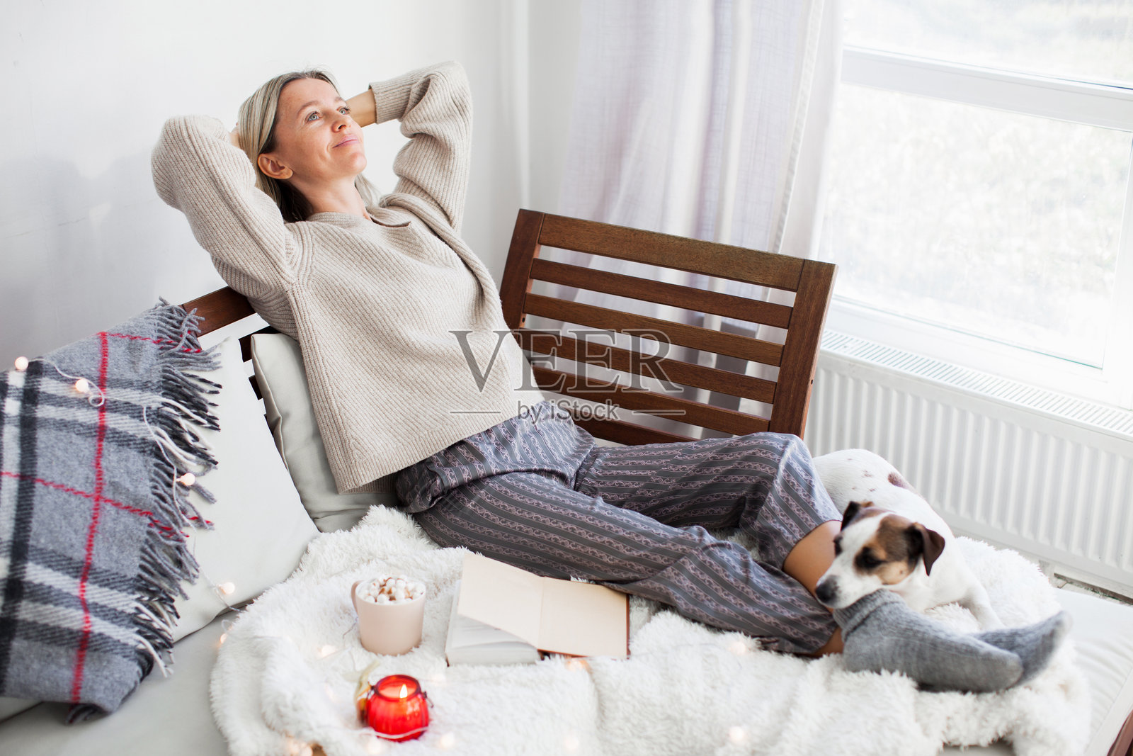 宁静的家庭主妇坐在沙发上，双手放在头后，享受在家的时光。照片摄影图片