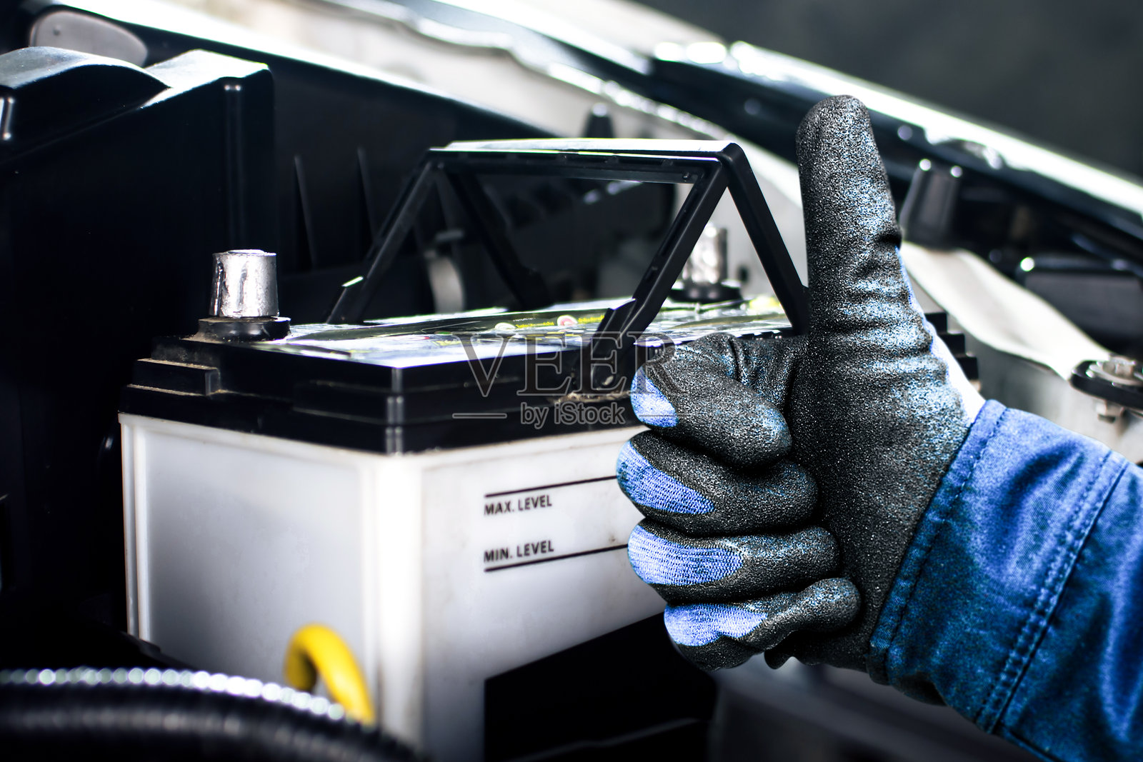 汽车修理工自信地竖起大拇指，站在汽车电池旁边照片摄影图片