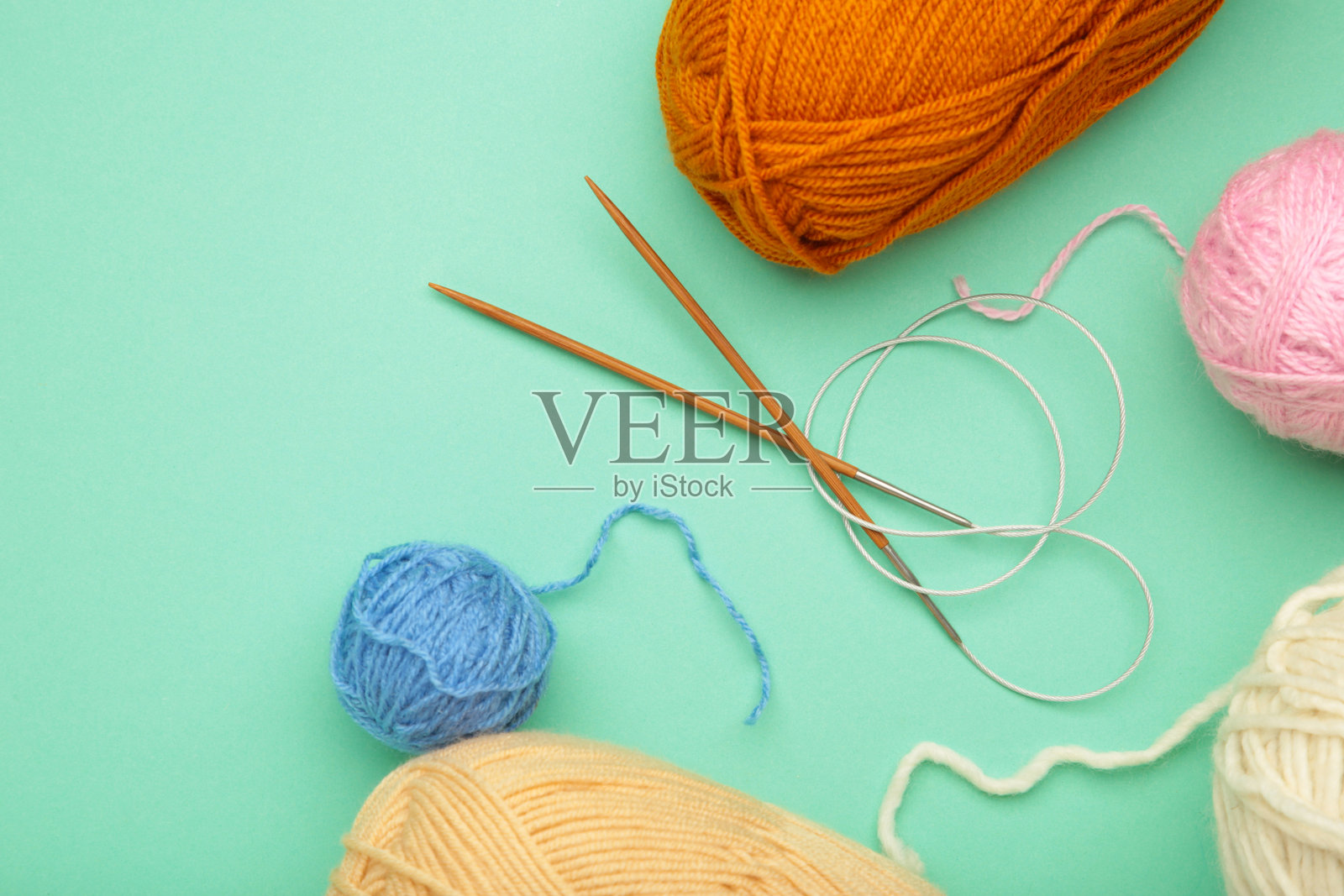 不同颜色的纱线和针织针在薄荷色背景上。秋天。照片摄影图片