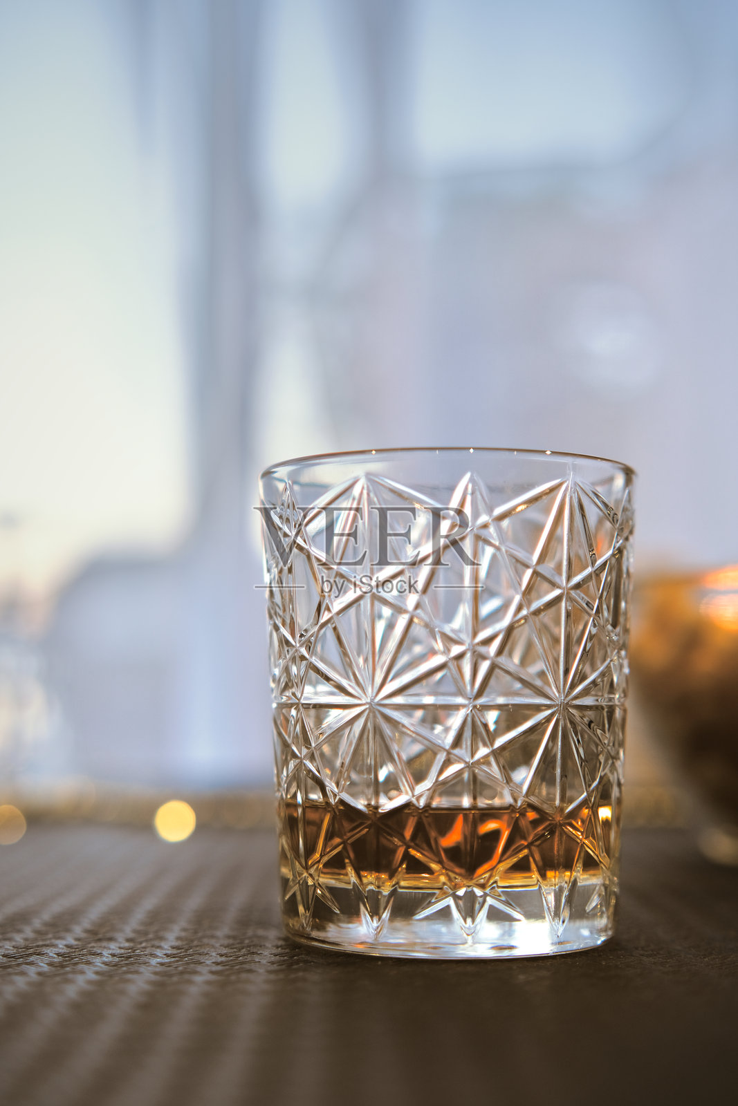 水晶玻璃杯中盛着威士忌，放置在桌子上，透过光线照射。照片摄影图片