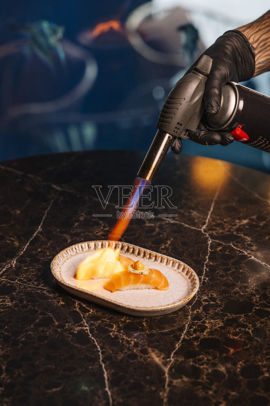 厨师用烹饪喷枪小心地炙烤握寿司的特写镜头。照片摄影图片