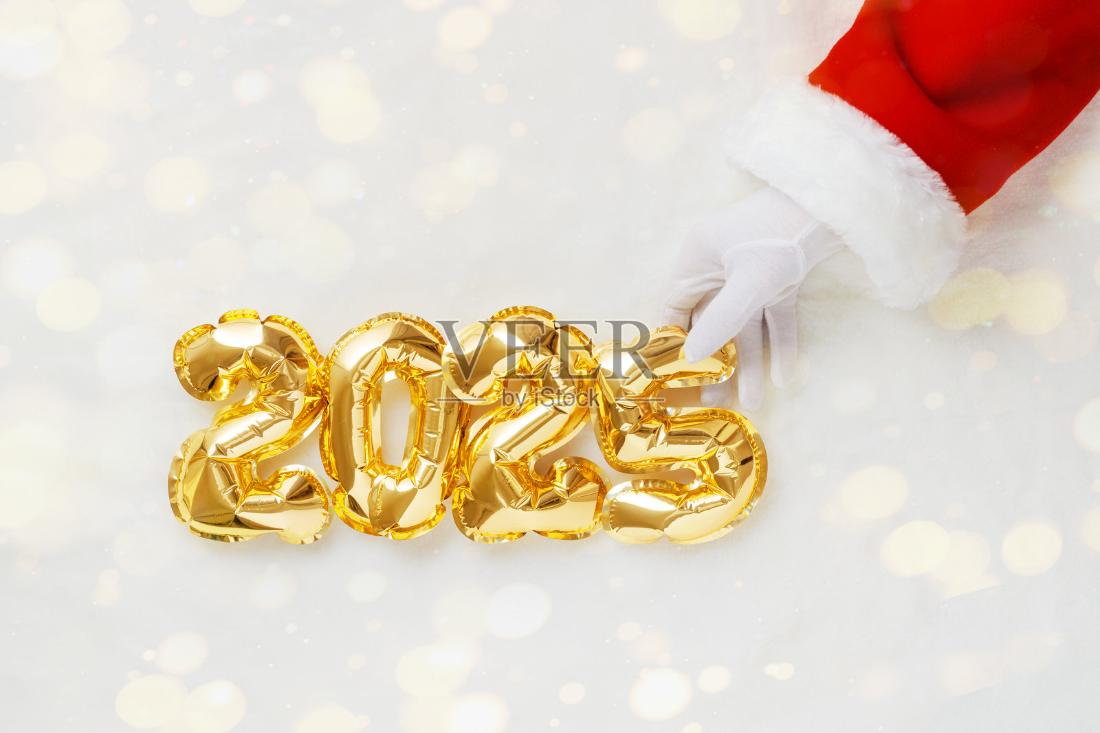 圣诞老人手持金色铝箔气球数字2025，背景为白色毛皮，柔和的金色散景灯光，圣诞节和新年庆祝概念，俯视图，冬季假日极简美学照片摄影图片