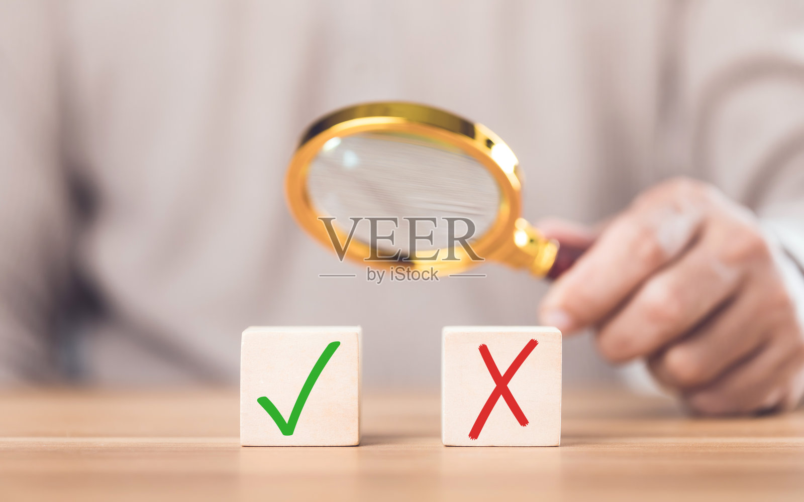 一名男子用放大镜观察木块上的对勾和“X”符号。该图像反映了从错误中选择正确的概念，突出了谨慎的决策和评估。照片摄影图片
