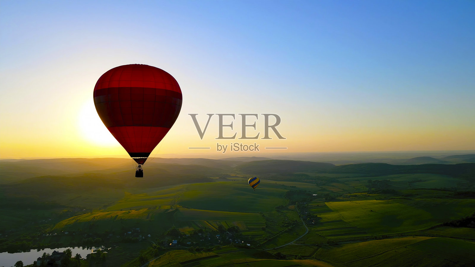 日落时分，红色热气球在美丽的风景上空飘浮。一个令人惊叹的景象，红色热气球在广阔的绿色景观上空飞翔。照片摄影图片