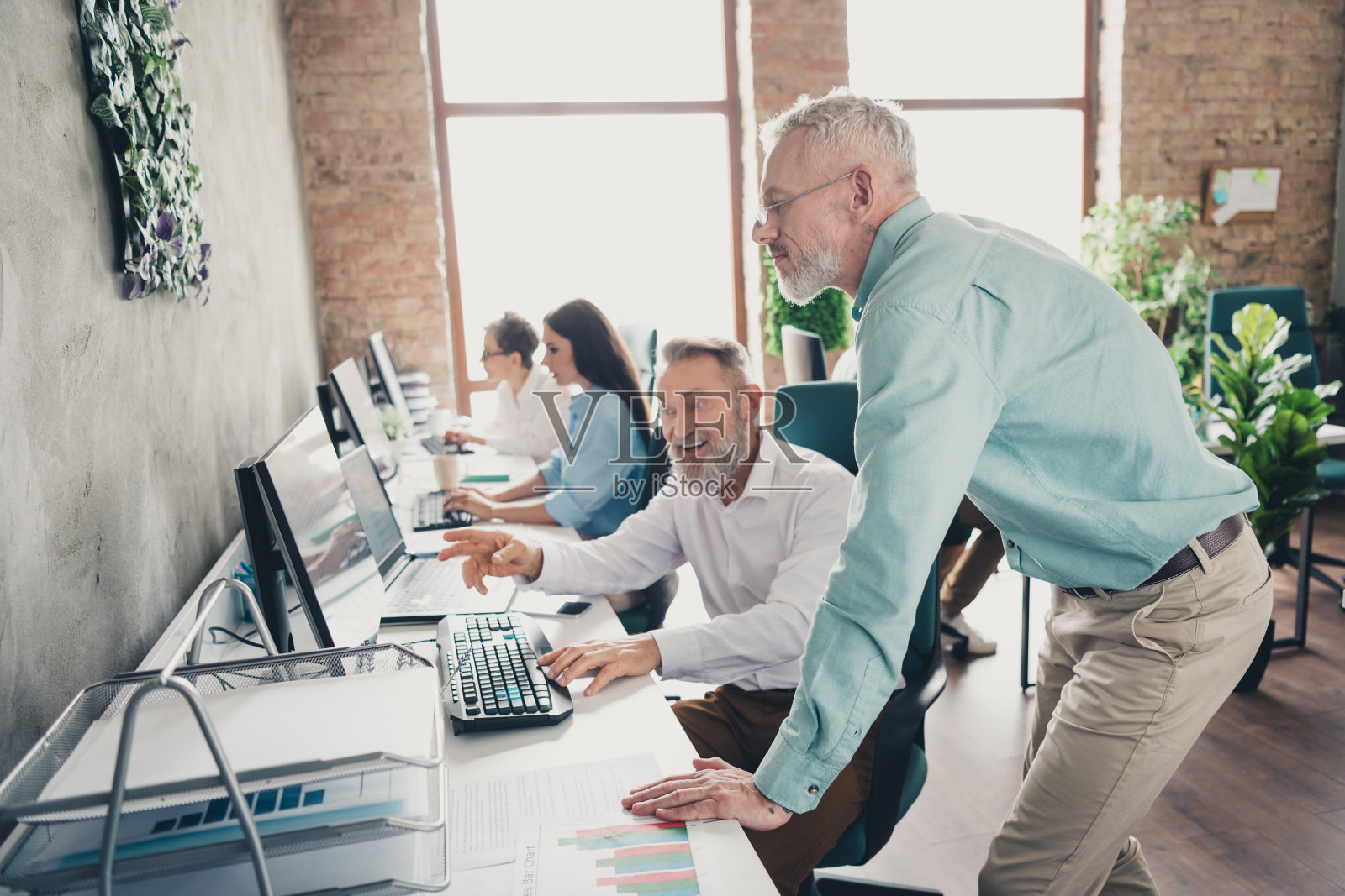 成熟男性在明亮的办公室中共同工作，参与会议，进行成功的团队合作项目。照片摄影图片