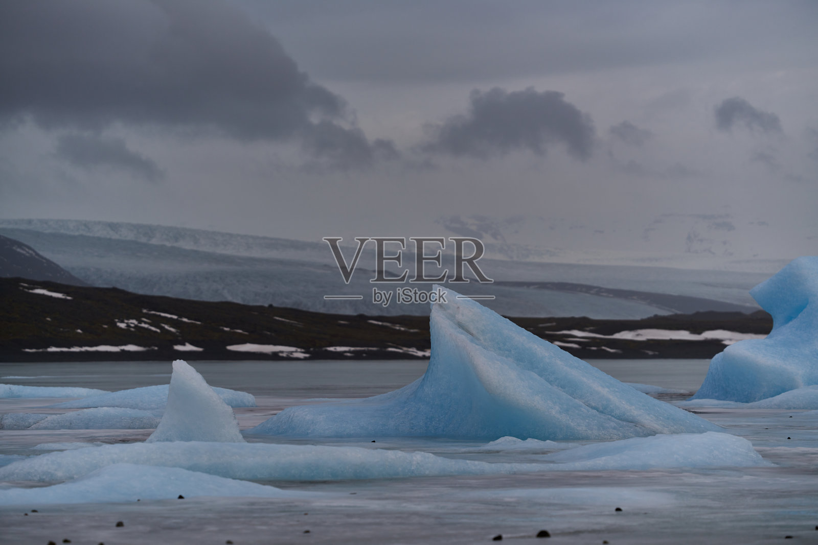 蓝色冰山漂浮在水面上，天空多云照片摄影图片