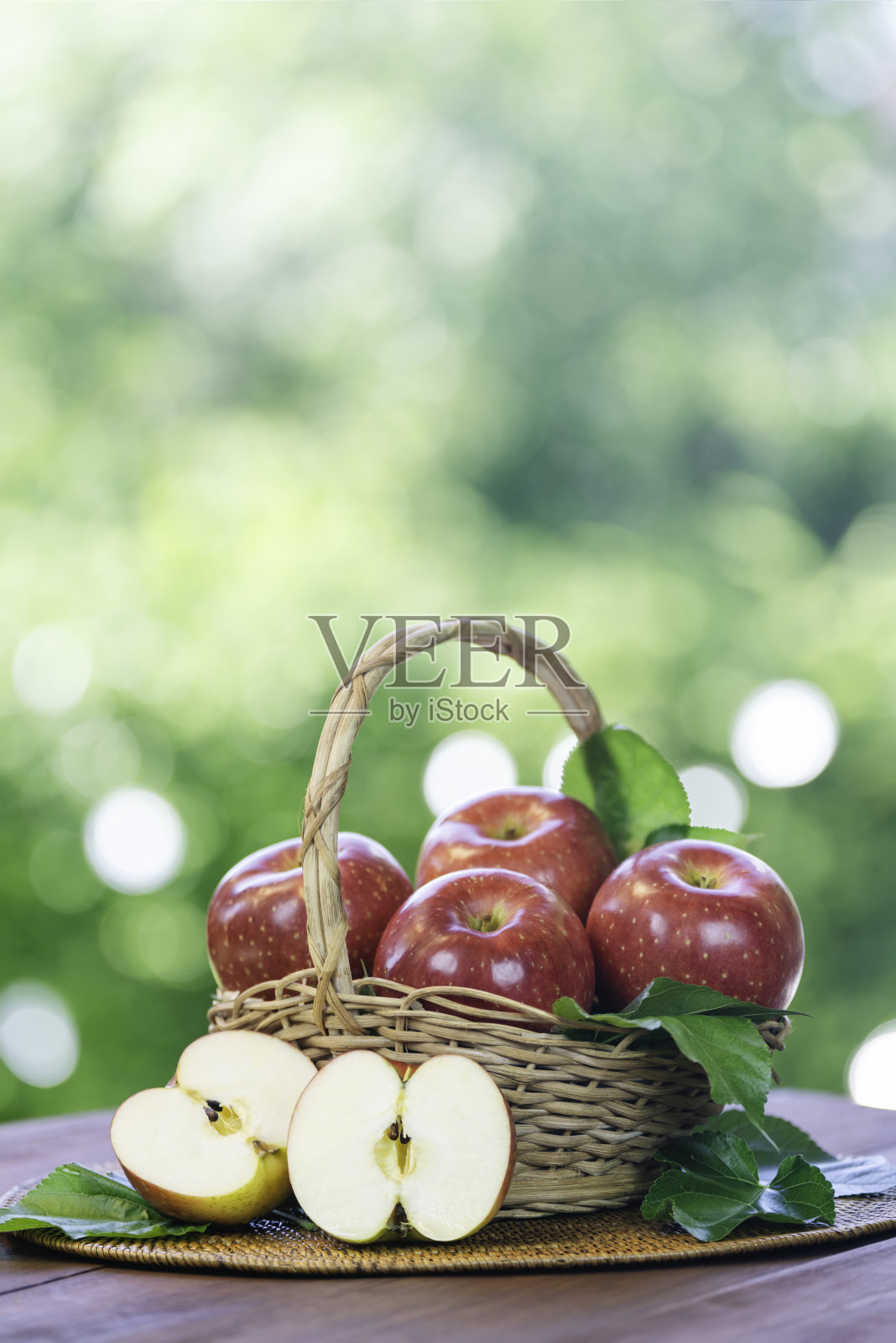 篮子里的红苹果，背景是模糊的绿色植物；花园里的木桌上放着红色日本苹果的篮子。照片摄影图片