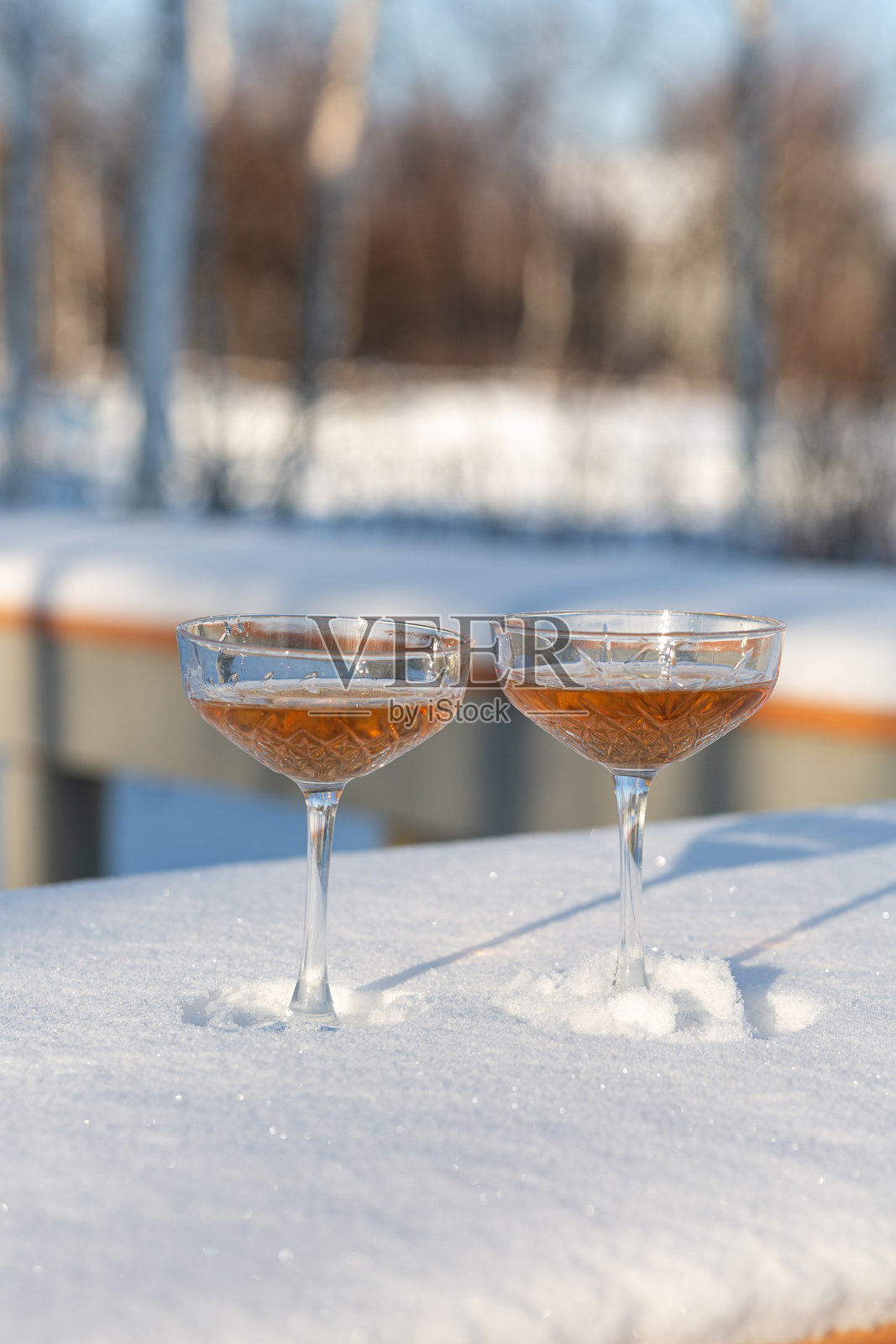 两杯香槟放在被雪覆盖的长椅上照片摄影图片